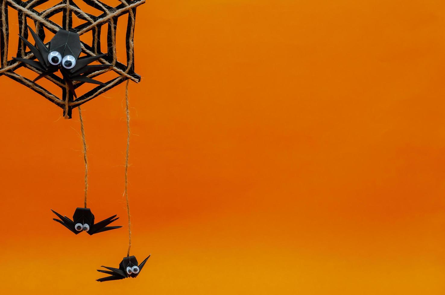 The origami Halloween background of spiders hanging on cobweb isolated on orange background. photo