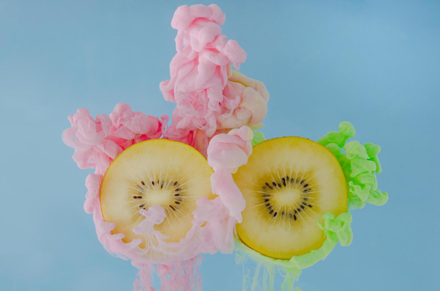 Slice kiwi fruits with partial focus of dissolving pink and green poster color in water photo