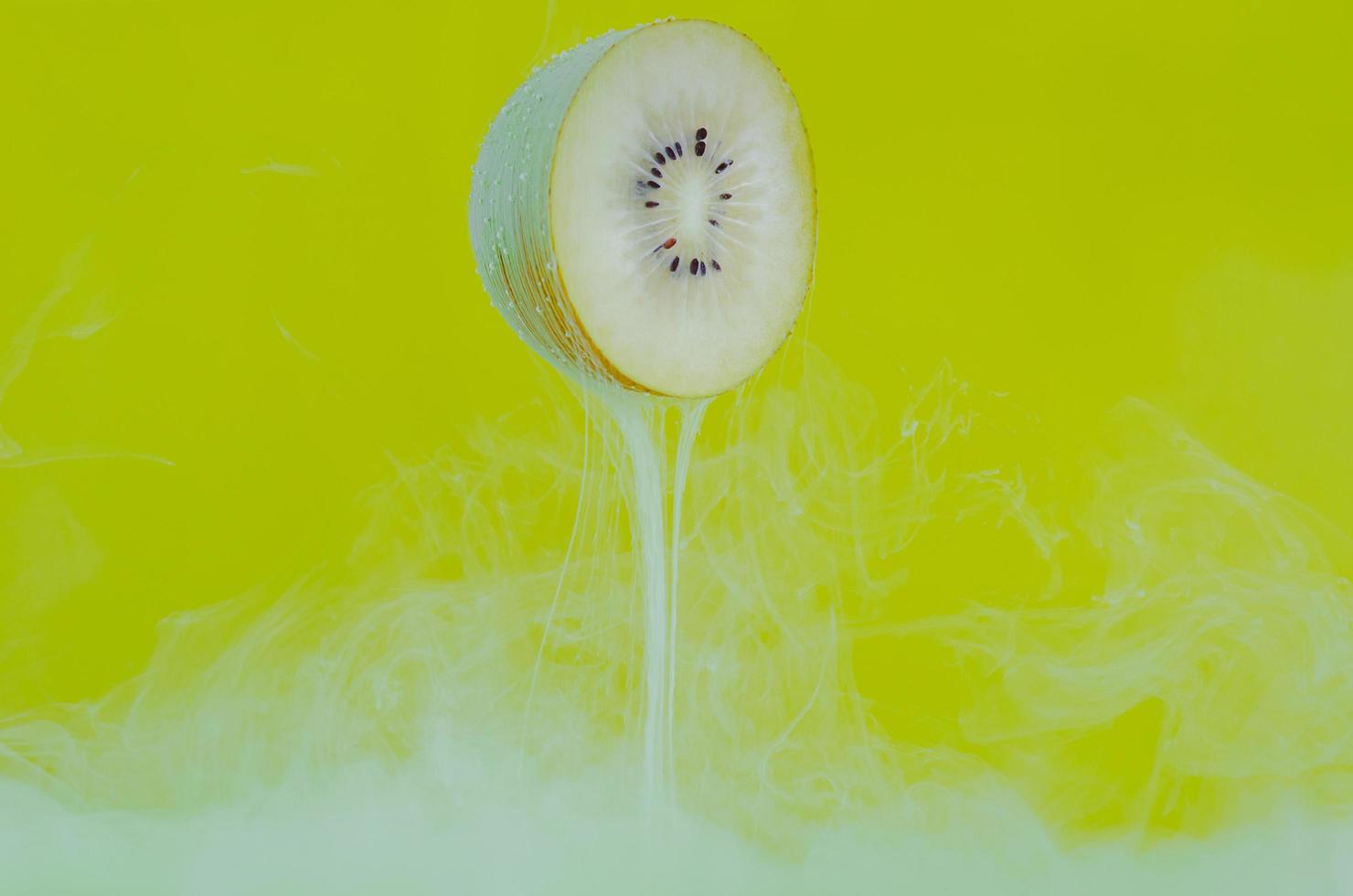 Blurred focus of dissolving green poster color in water with slice kiwi fruit on yellow background photo