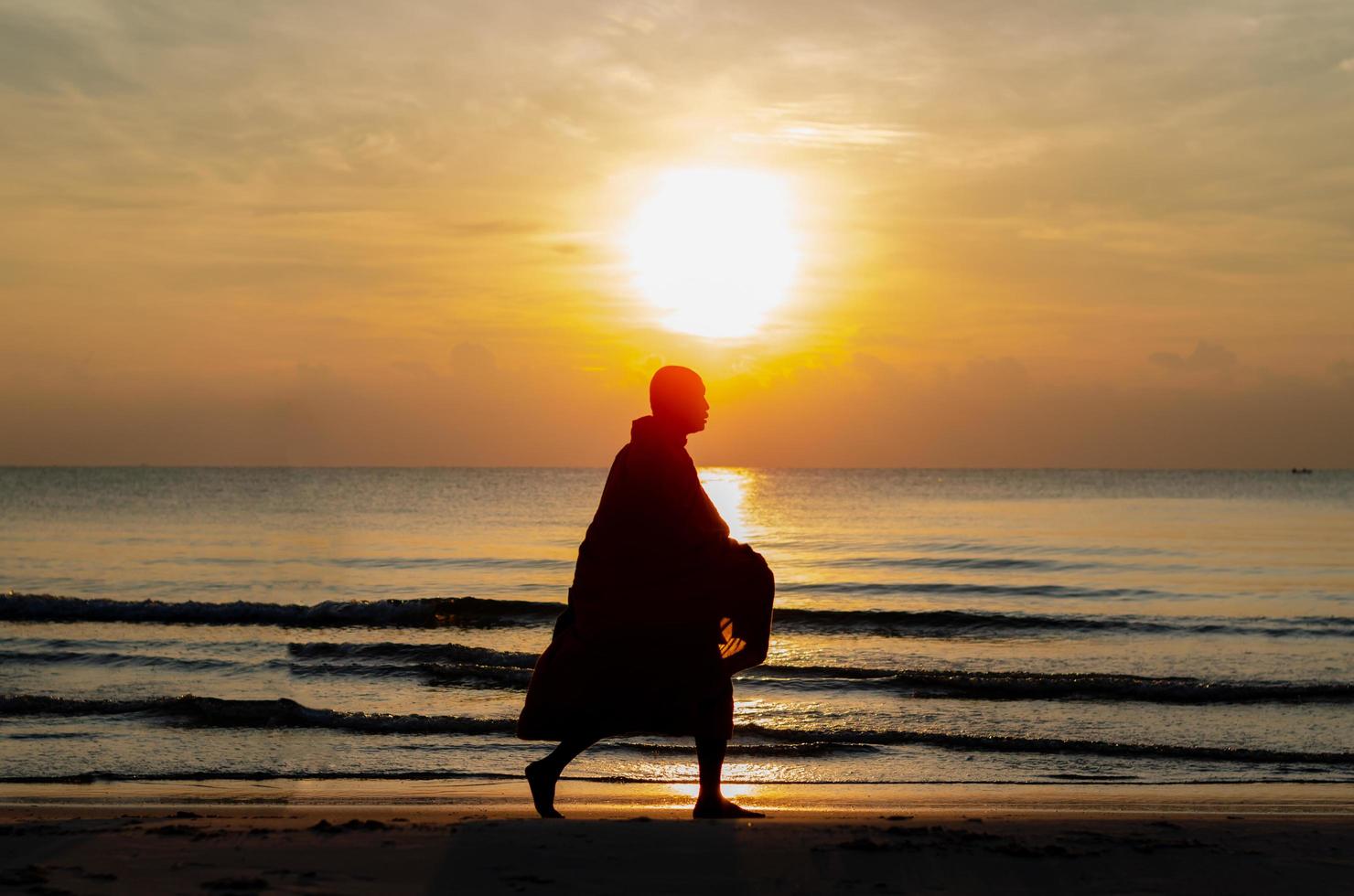 Sunrise with reflection on the sea and beach that have silhouette photo of buddhist monk.