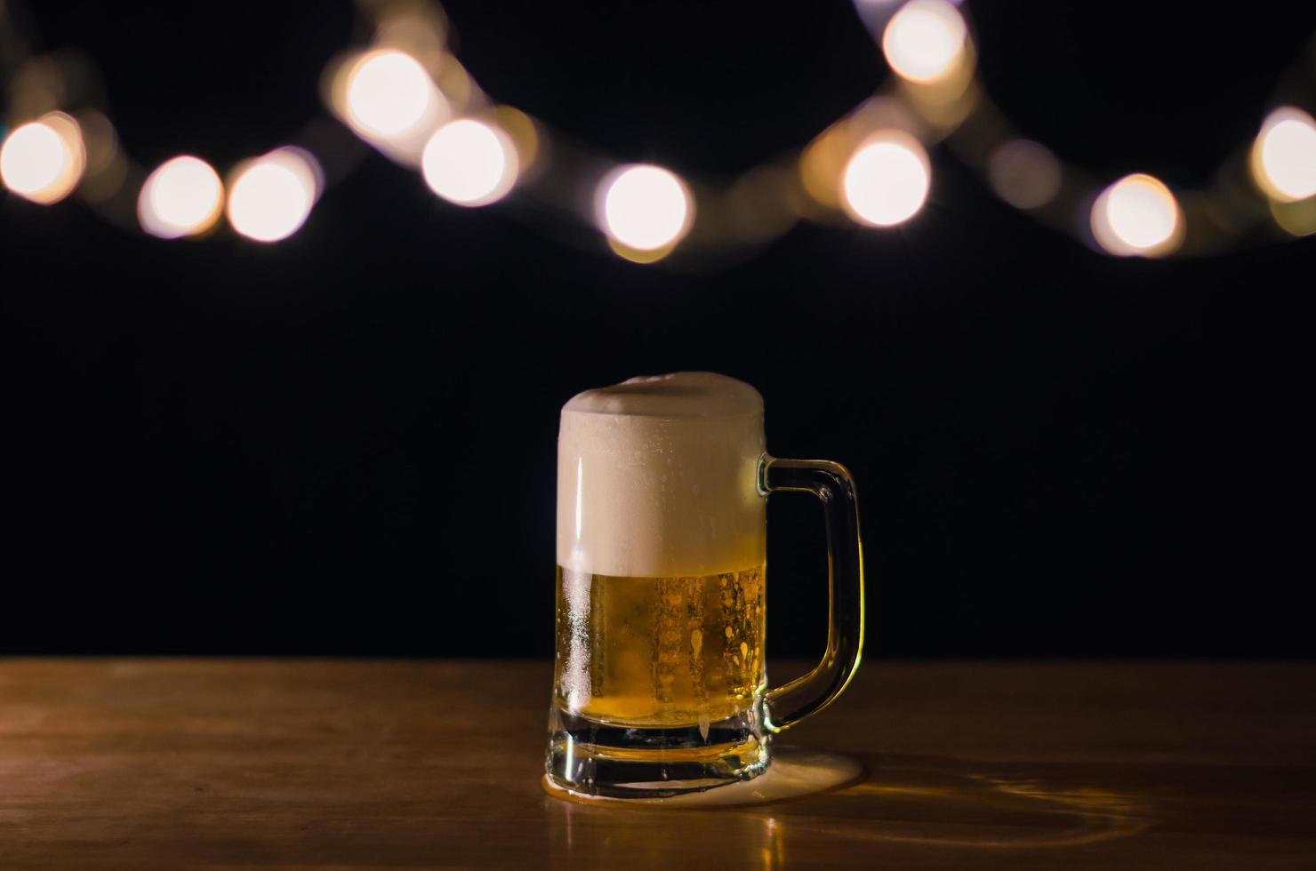 un vaso de cerveza sobre una mesa de madera que tiene luces bokeh en la parte superior con un fondo oscuro. foto