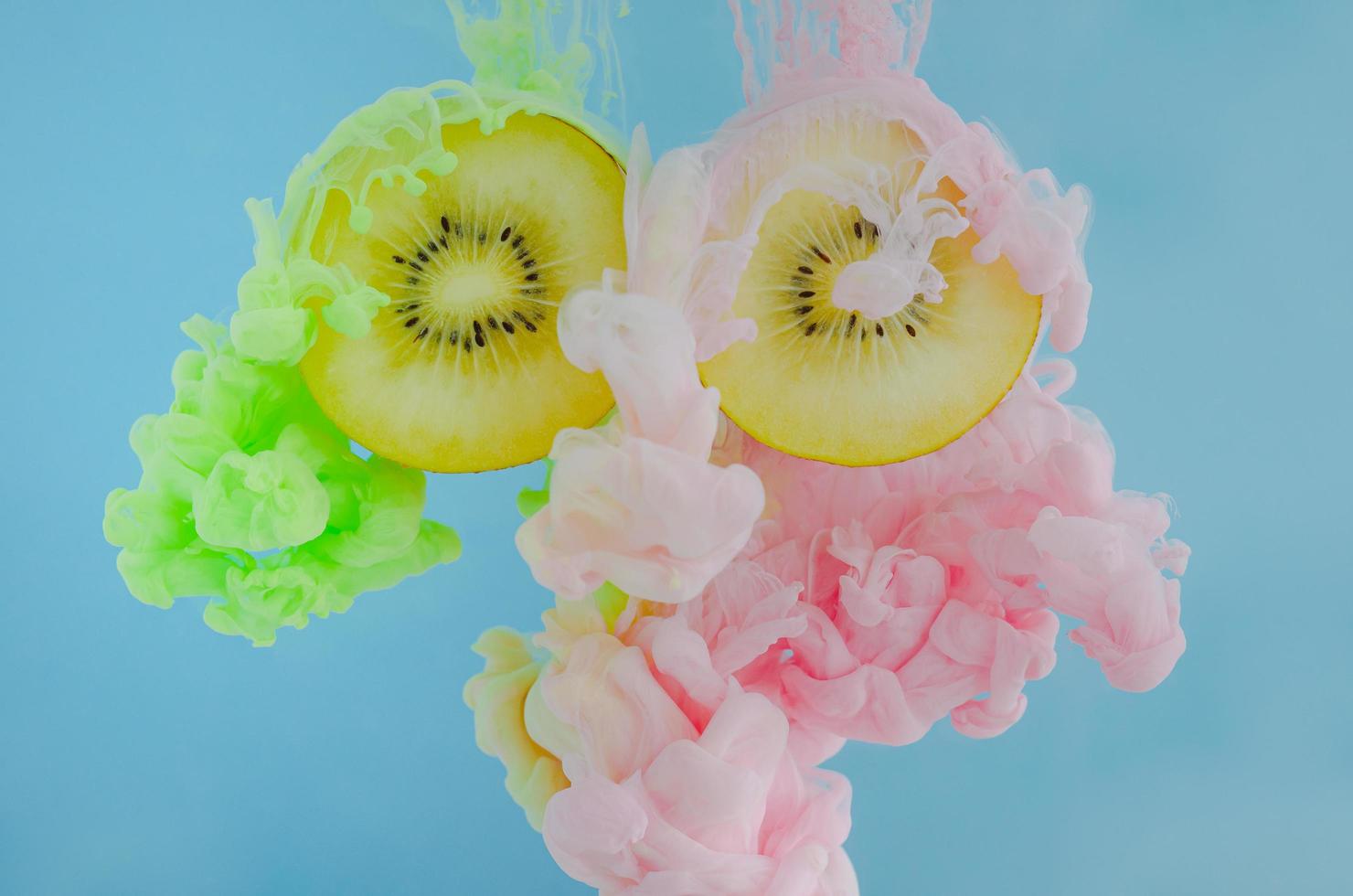 Slice kiwi fruits with partial focus of dissolving pink and green poster color in water on blue background photo