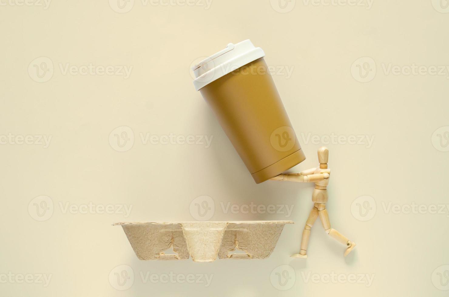 Wooden model holding reuse coffee tumbler to put on recycle paper tray. World environment day concept. photo