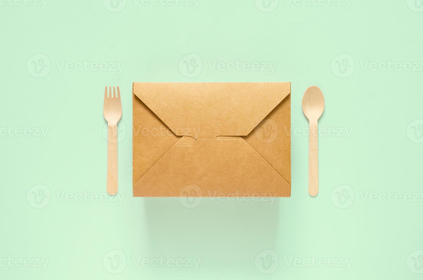 Disposable, compostable paper food box, fork and spoon on green background for world environment day concept. photo
