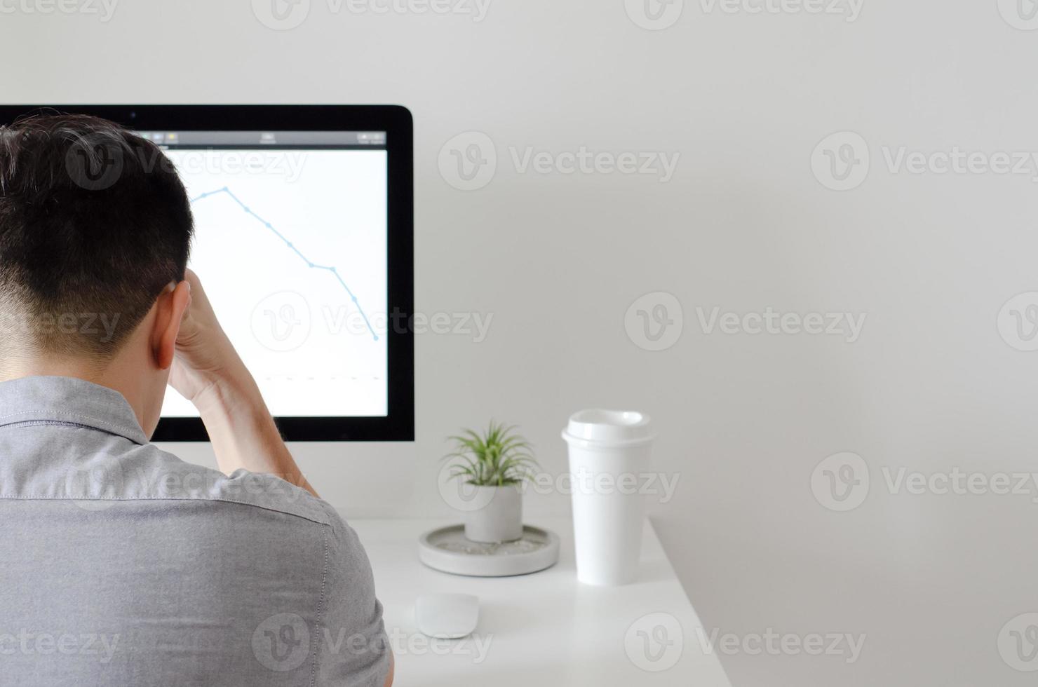 A person working with serious expression at office with personal computer screen that have a coffee and tillandsia air plant with space for text on white wall for working and office concept. photo