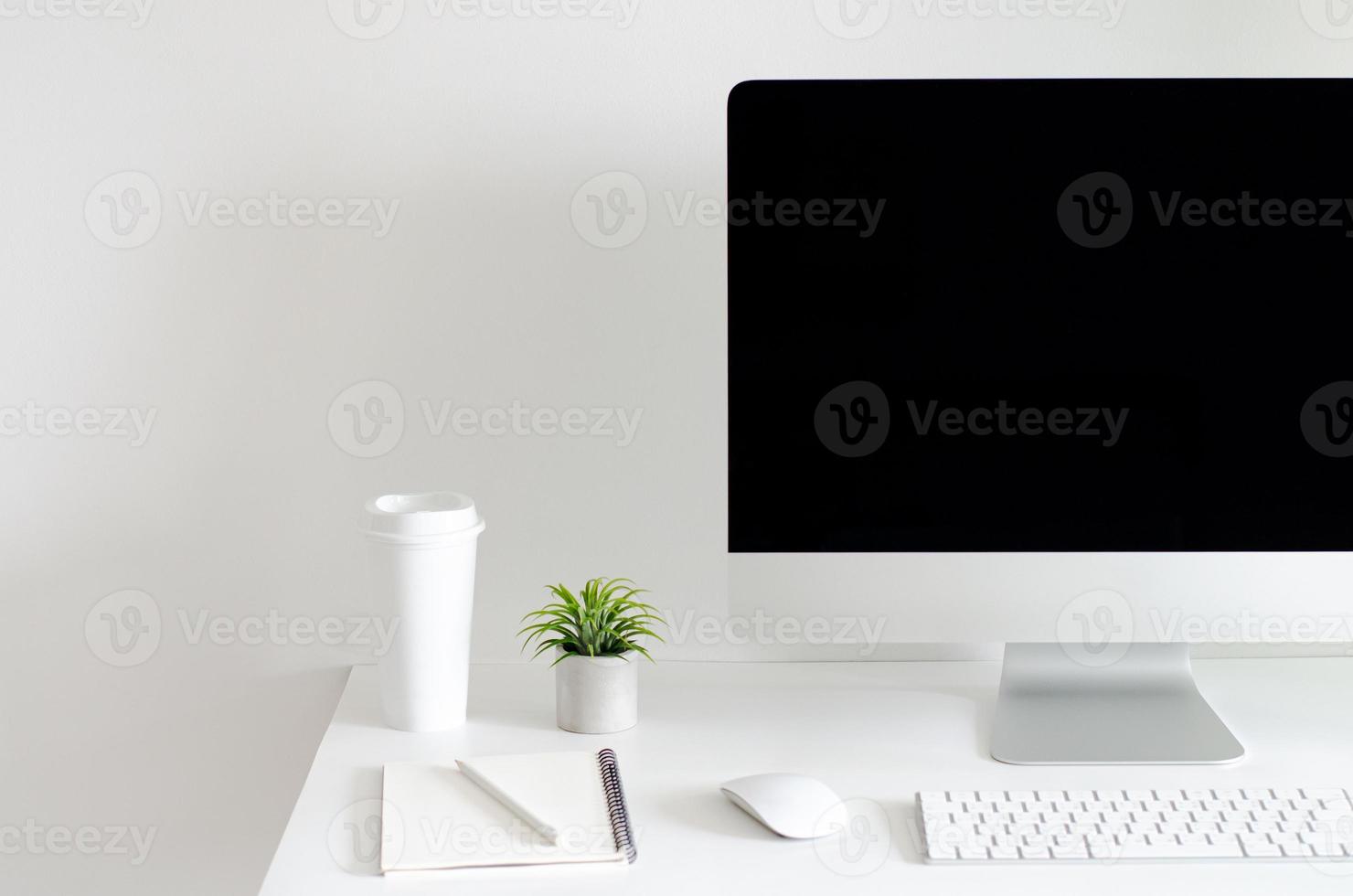 Modern personal computer screen on white table with a cup of coffee and Tillandsia air plant with space for text on white wall for working and office concept. photo