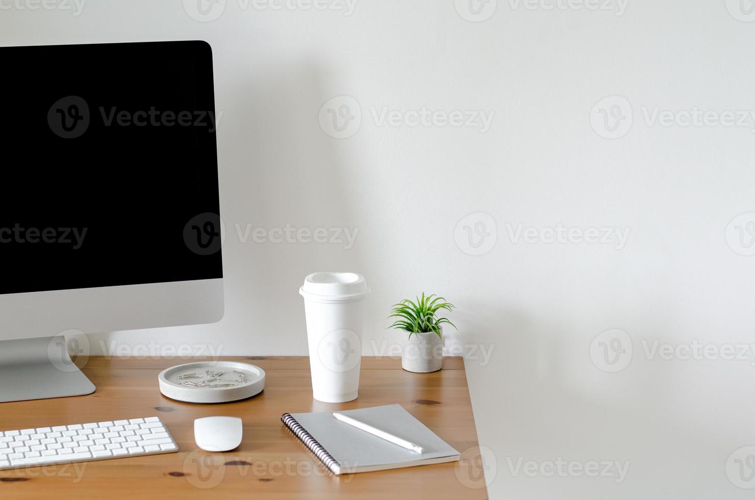 Modern personal computer screen on wooden table with a cup of coffee and Tillandsia air plant with space for text on white wall for working and office concept. photo