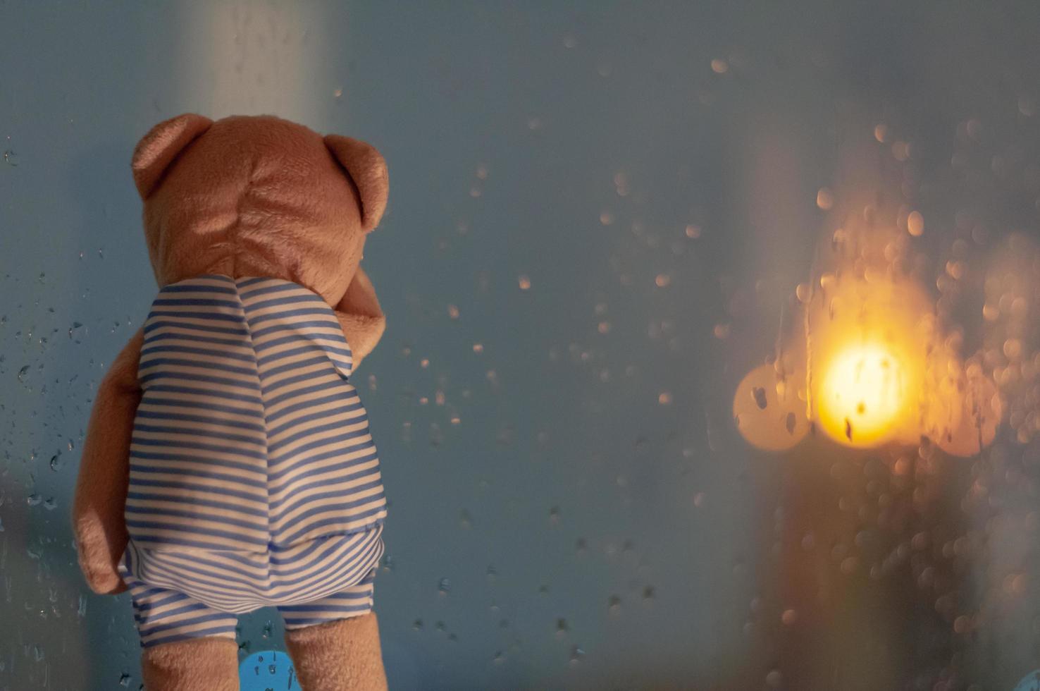 Sadly Teddy Bear crying at window in rainy day. photo