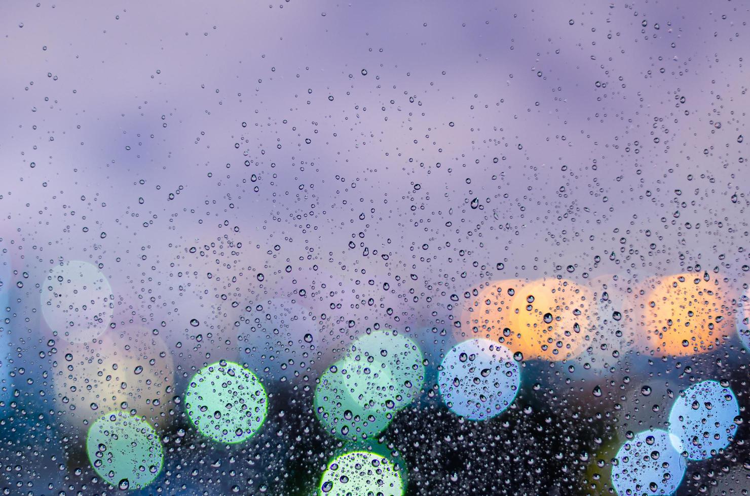 gota de lluvia en la ventana de vidrio en la temporada del monzón con luz de bokeh colorida del fondo de los edificios de la ciudad. foto