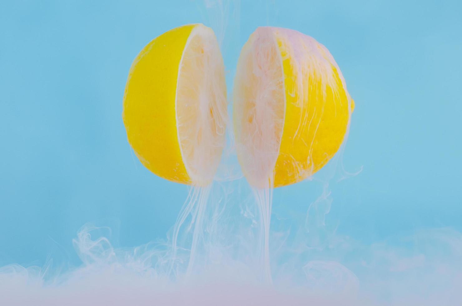 enfoque borroso de disolver el color rosa del afiche en una gota de agua entre dos rodajas de limones sobre fondo azul foto