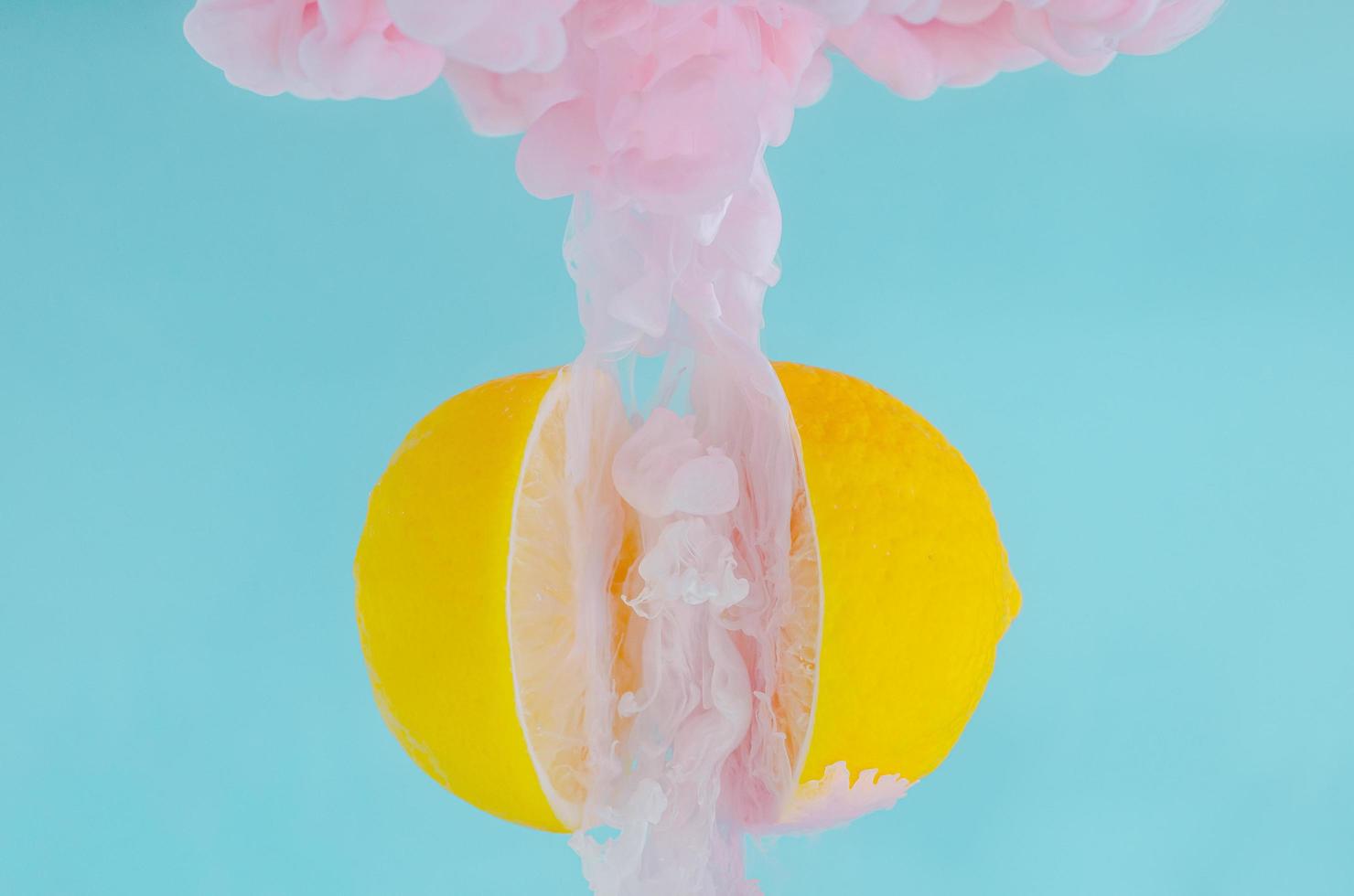 Partial focus of dissolving pink poster color in water between two slice lemons on blue background photo