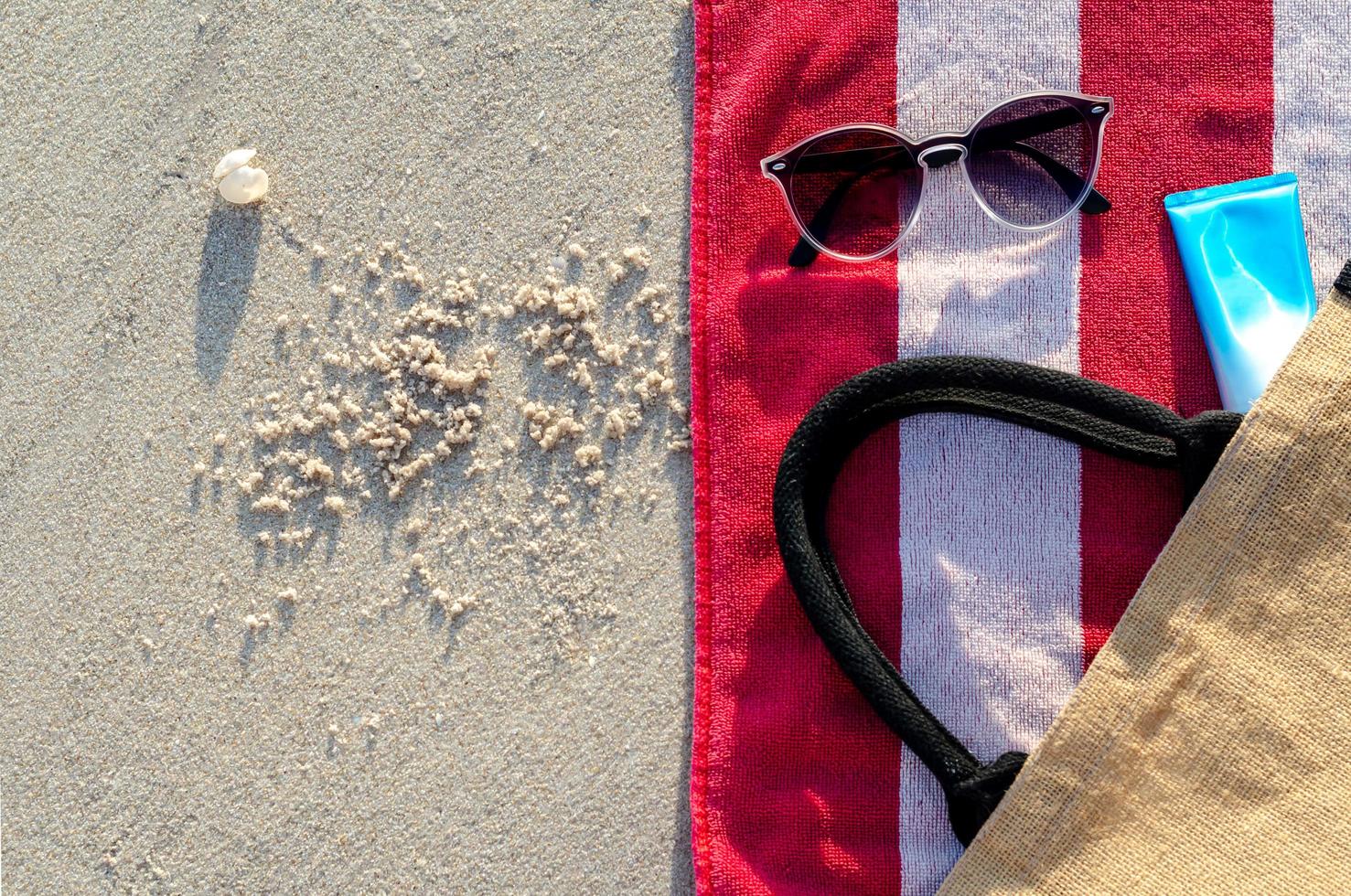 Sunglasses with sunscreen lotion and bag on red towel. photo