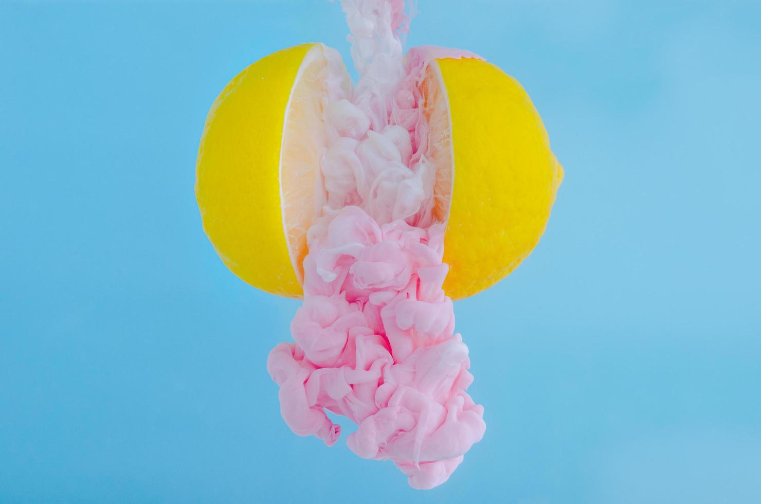 Partial focus of dissolving pink poster color in water drop between two slice lemons on blue background for summer, abstract and background concept. photo