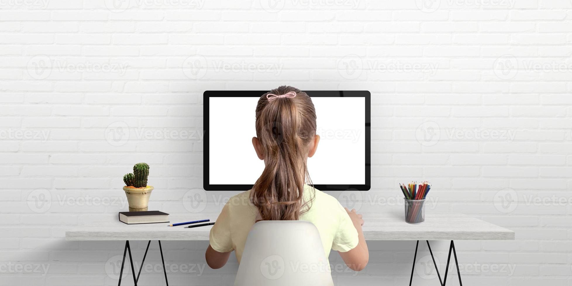 Girl is studying and working on the computer. The concept of using modern technologies for children. Work desk in the room with books and pens photo