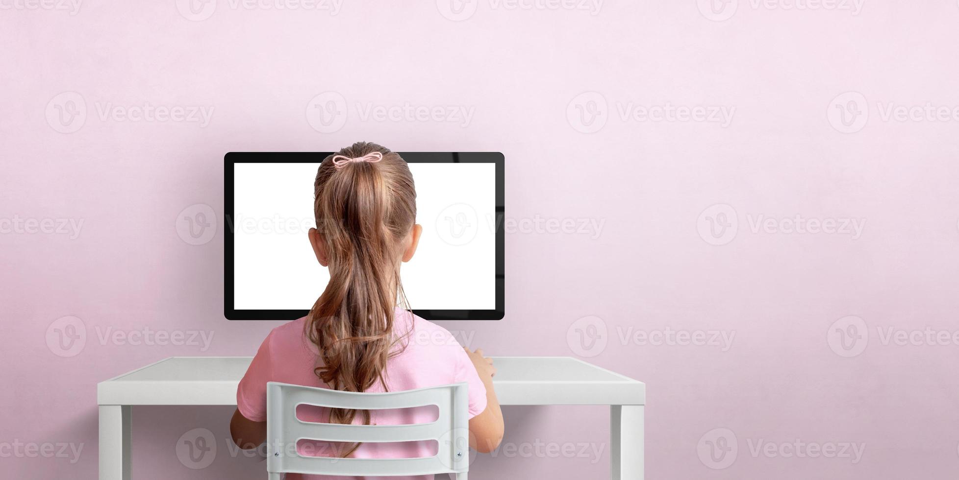 Girl sitting on a chair and working on the computer. Isolated computer display for design promotion. Pink wall with copy space photo