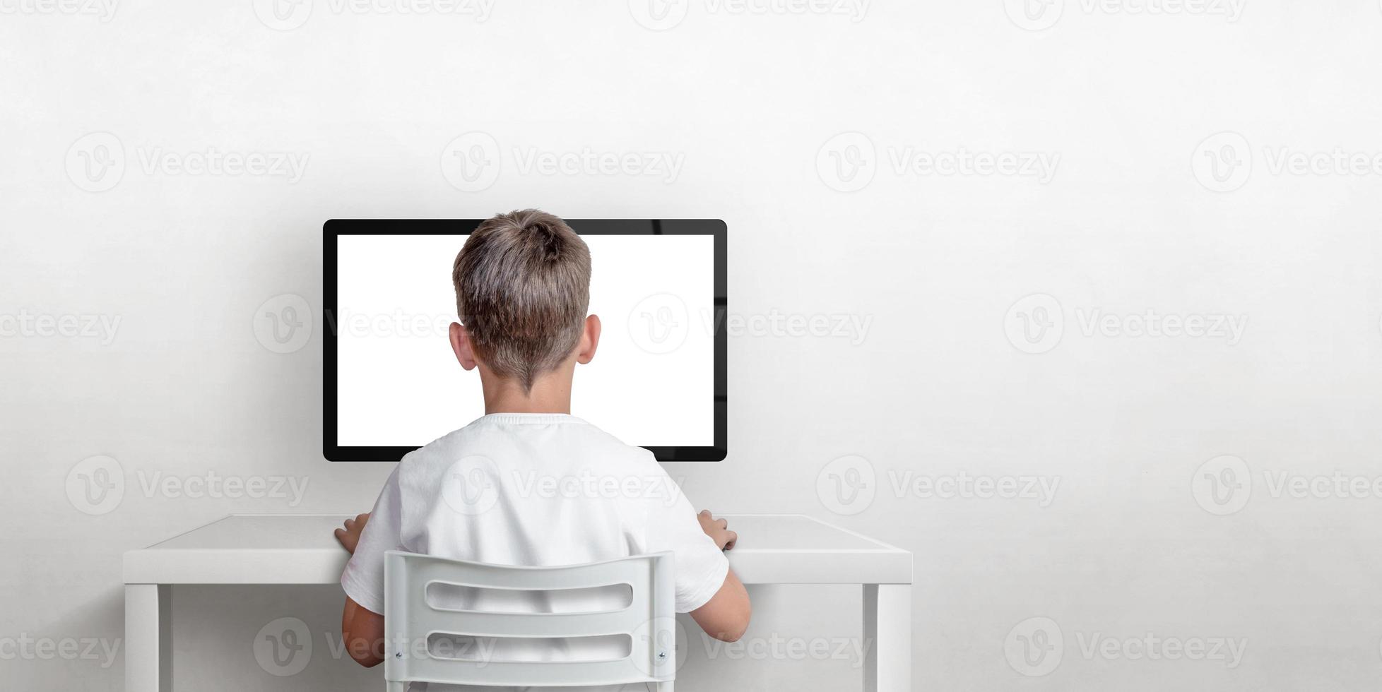 Boy is working on the computer, his back is turned. Isolated computer display for mockup. Copy space on the wall. The concept of working and learning on the computer photo