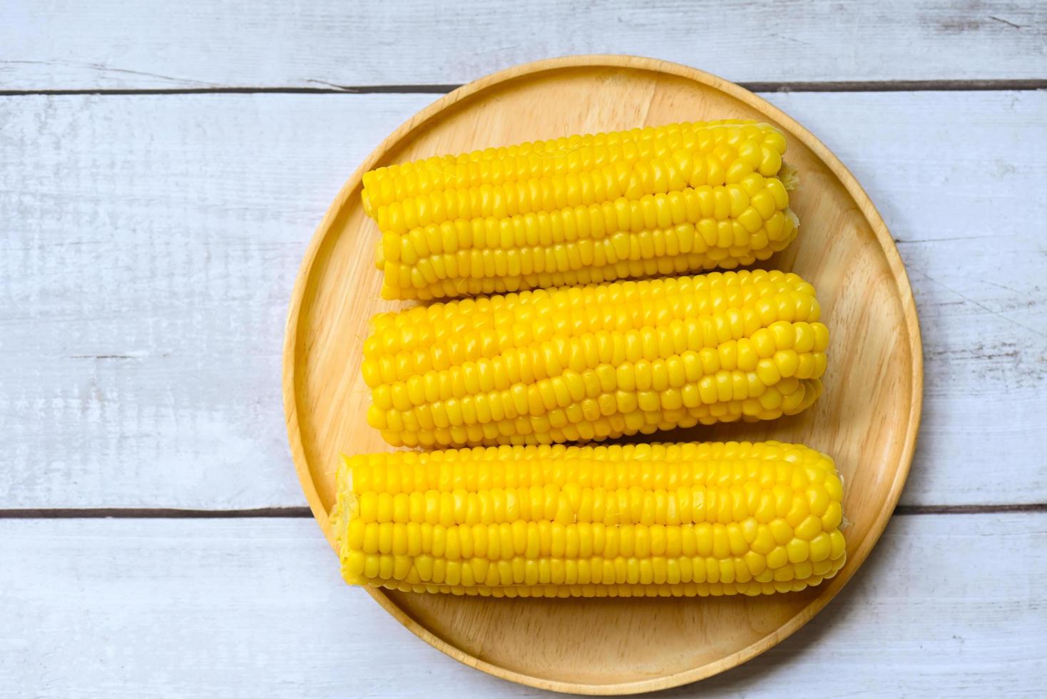 sweet corn cooked on wooden plate background, ripe corn cobs steamed or boiled sweetcorn for food vegan dinner or snack - top view photo