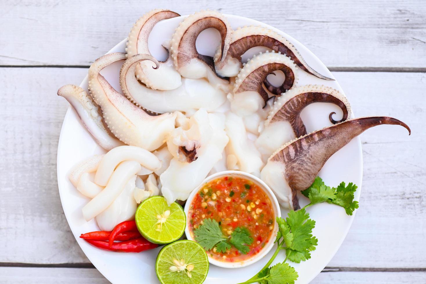 plato de mariscos comida de calamar en un plato blanco, calamar fresco cocido al vapor hervido con ensalada de verduras lima limón y salsa de mariscos salsa de chile servido en la mesa, tentáculos de pulpo sepia océano gourmet foto