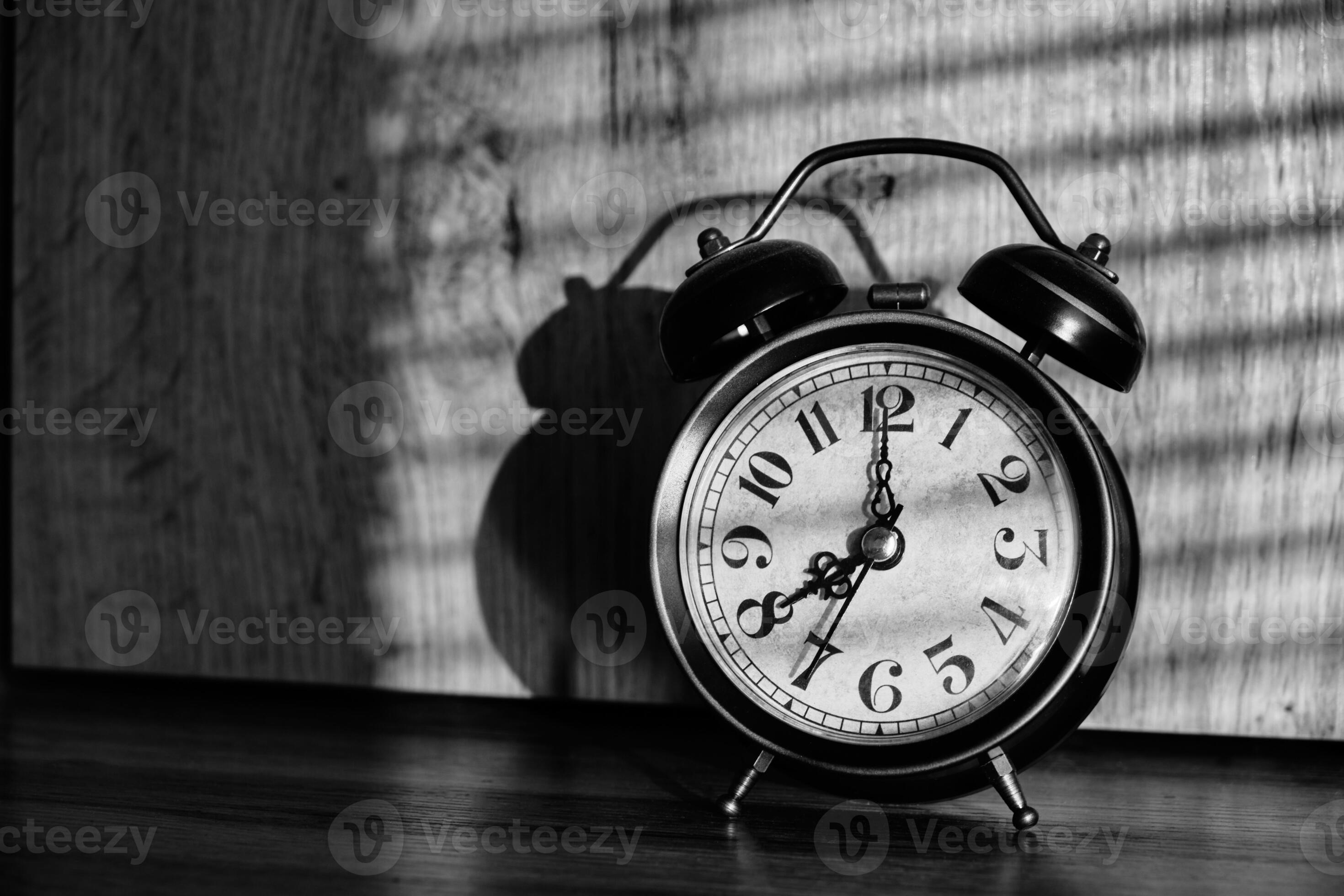 Old retro alarm clock early morning table, shadows from blinds in