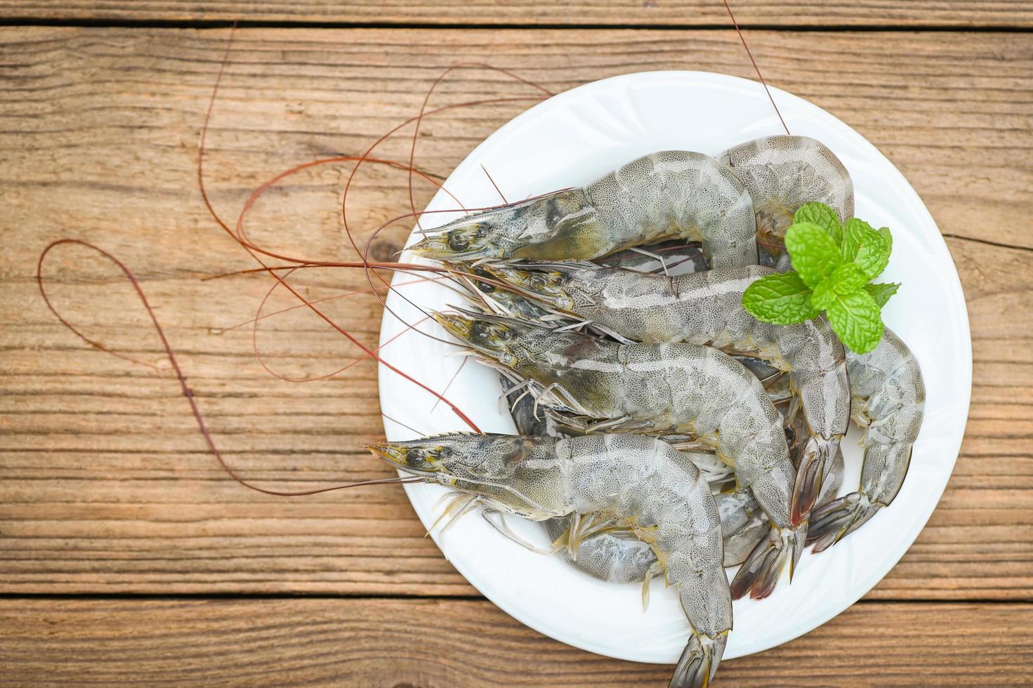 camarones crudos en plato blanco con hojas de menta y camarones fondo de madera para cocinar, cerrar camarones o langostinos frescos, marisco estante - vista superior foto