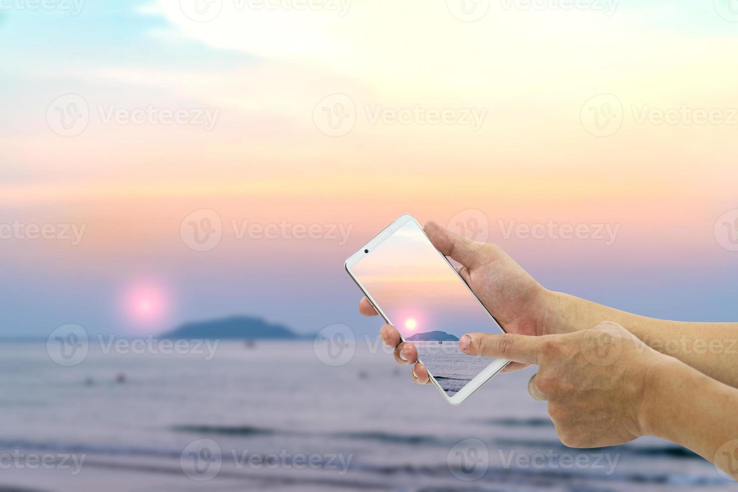 hand holding mobile smart phone with front the beach and sky  background photo