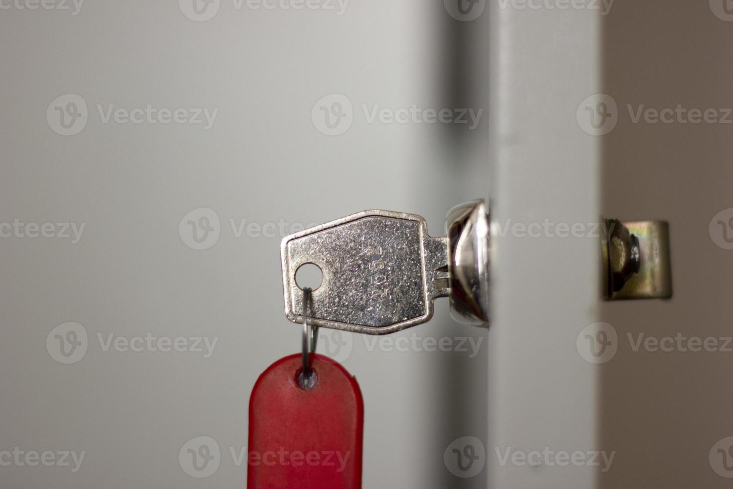 Metal office key with red fob in lock closeup, horizontal photo on blurred background. Open door with key, safety system for document files and information