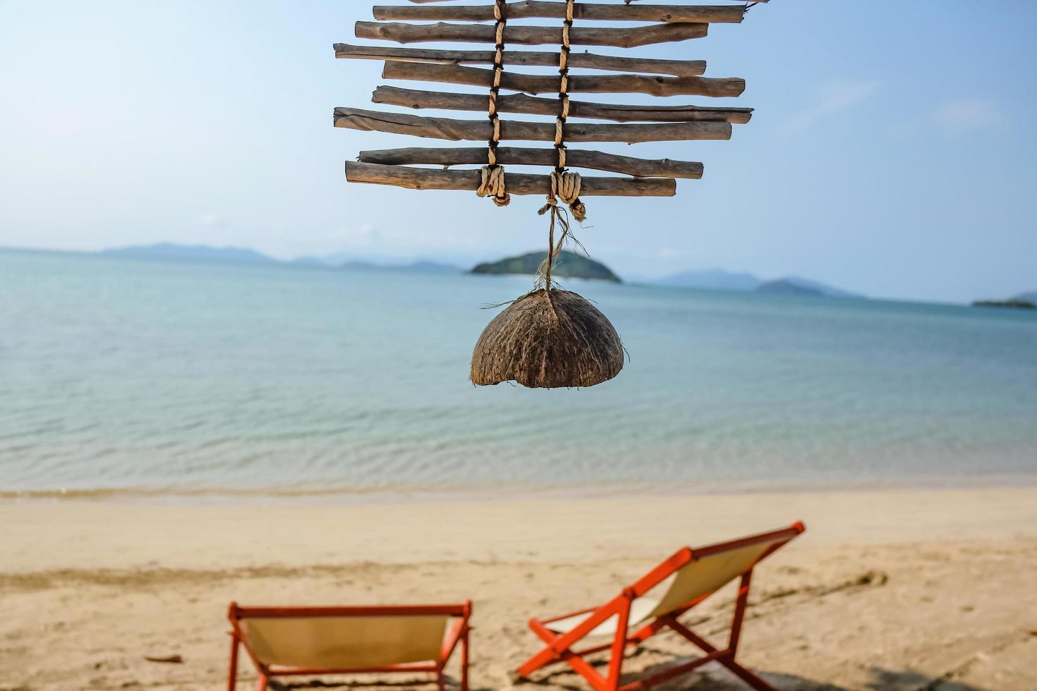 cierre la cáscara de coco con un océano idílico y un hermoso cielo en vacaciones, silla de madera relájese en la playa, koh mak trat tailandia, concepto de verano foto