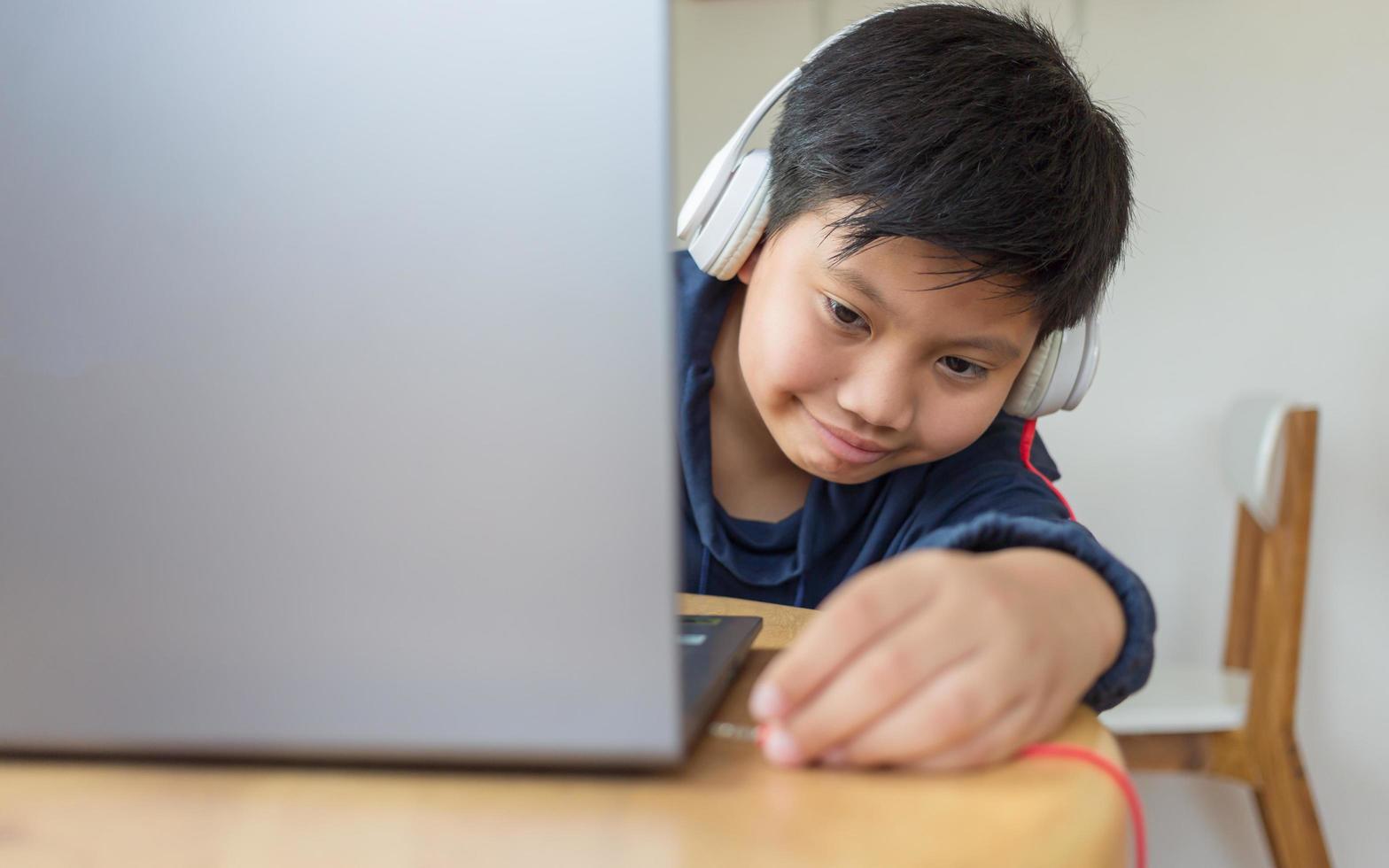 un chico lindo asiático se acerca para conectar sus auriculares a su computadora portátil solo con una cara que tiene la intención de usar la computadora para estudiar en línea en casa. enlazar y conectar foto