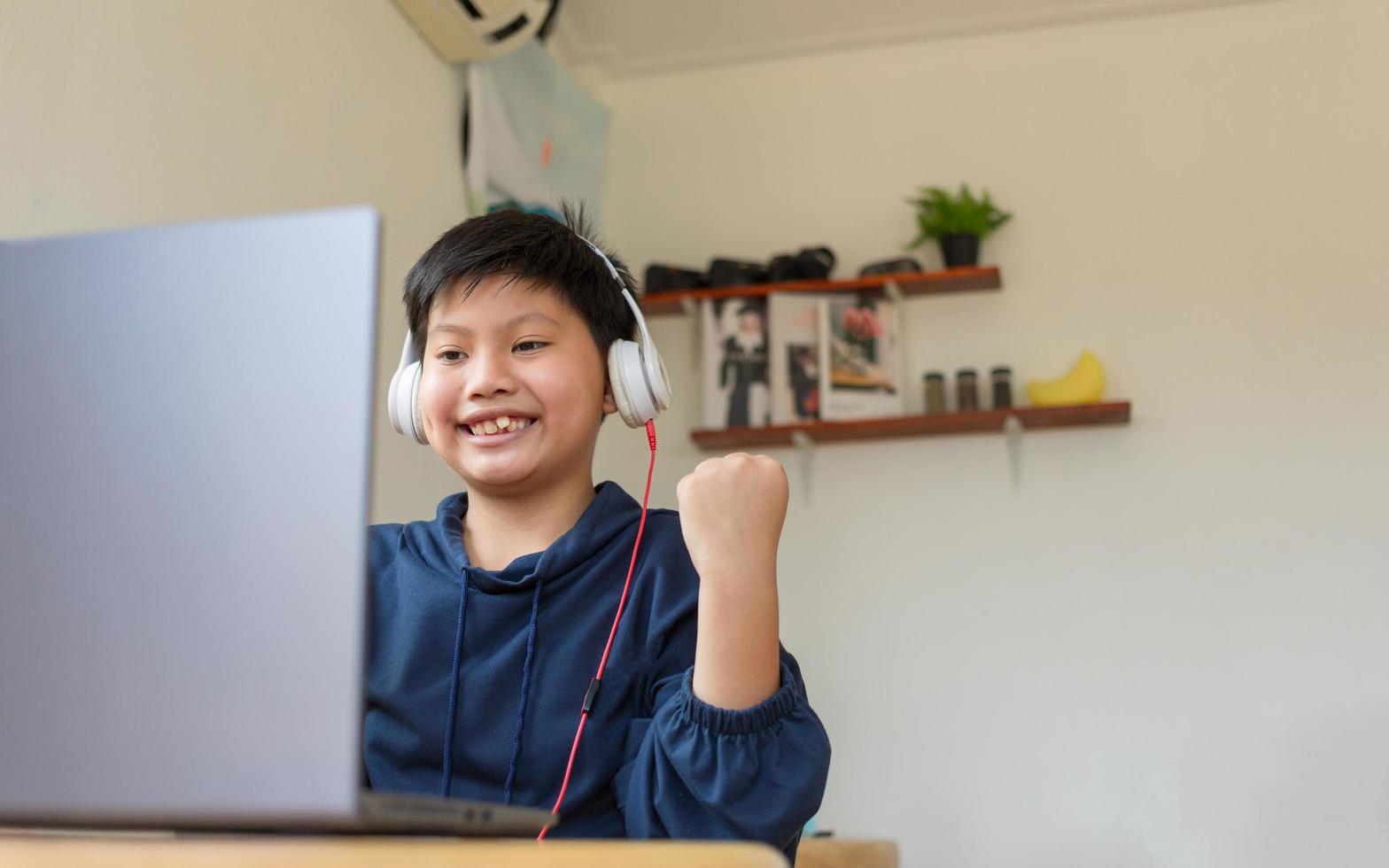 Smiling Asian young boy chatting with friends or a student studying the internet on social networks sitting in front laptop at home. Chat on Social Media and video conference. photo