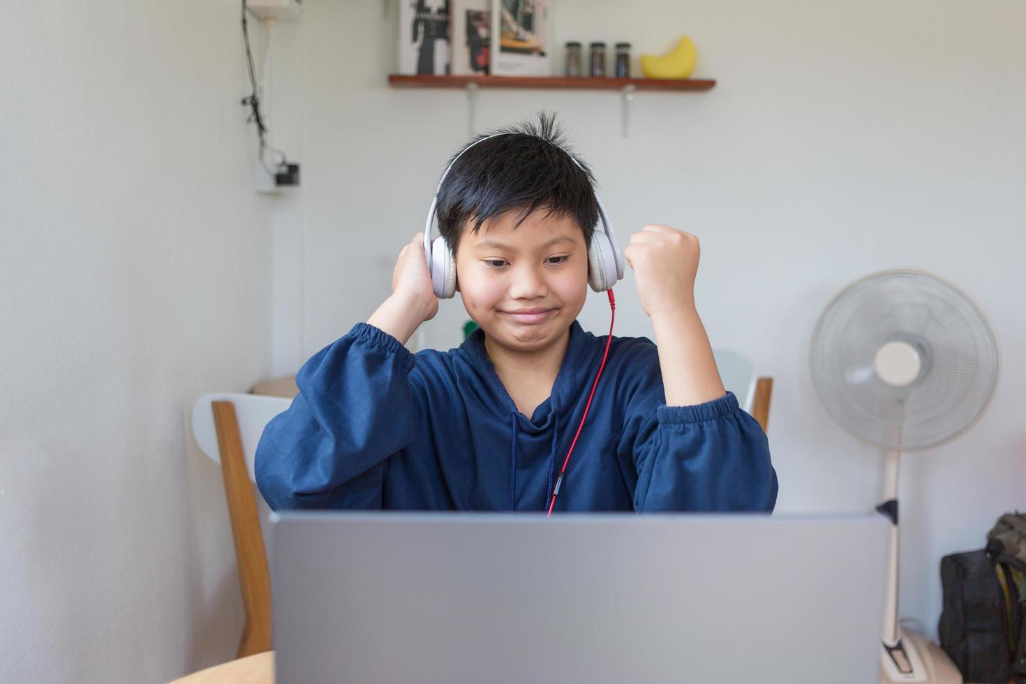 Smiling Asian young boy chatting with friends or a student studying the internet on social networks sitting in front laptop at home. Chat on Social Media and video conference. photo