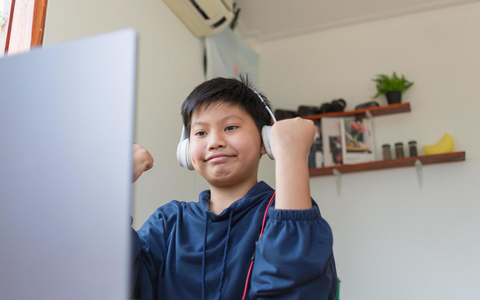 Smiling Asian young boy chatting with friends or a student studying the internet on social networks sitting in front laptop at home. Chat on Social Media and video conference. photo