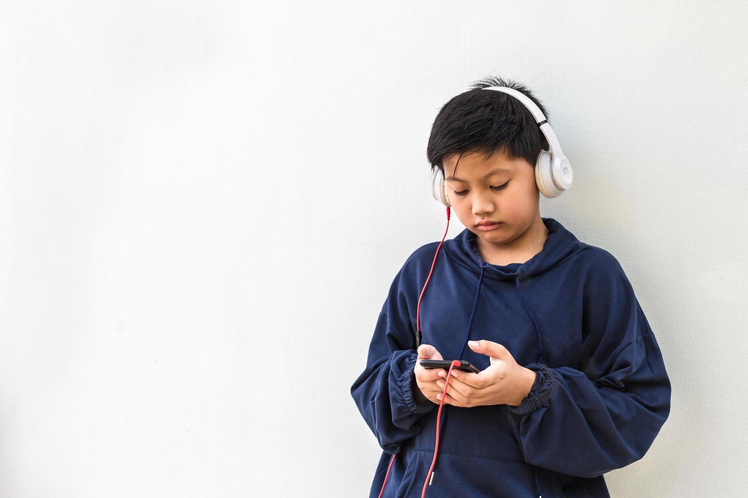 Cute Asian boy with white skin in a hoodie posing listening to the music on a mobile phone and headphones isolated over white background. portrait and copy space photo