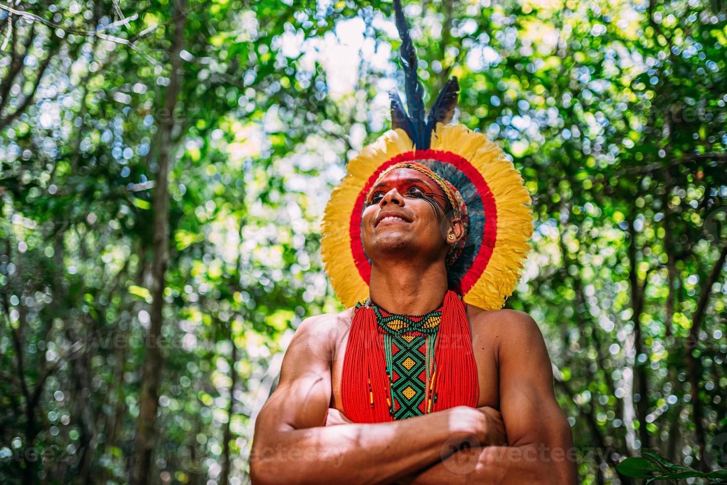 indio de la tribu pataxo, con tocado de plumas. joven indio brasileño mirando a la izquierda, sonriendo y con los brazos cruzados foto