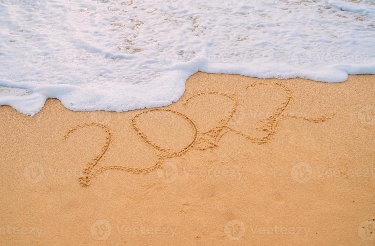 Closeup image of sea waves washing 2022 new year numbers from sand on the beach. Concept of New Year, Christmas and travel on winter holidays. photo