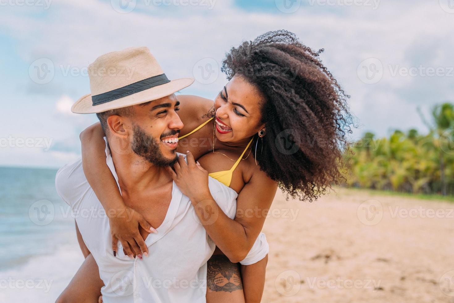 Pareja joven en vacaciones de verano en la playa, feliz hombre sonriente lleva a la mujer de vuelta al mar foto