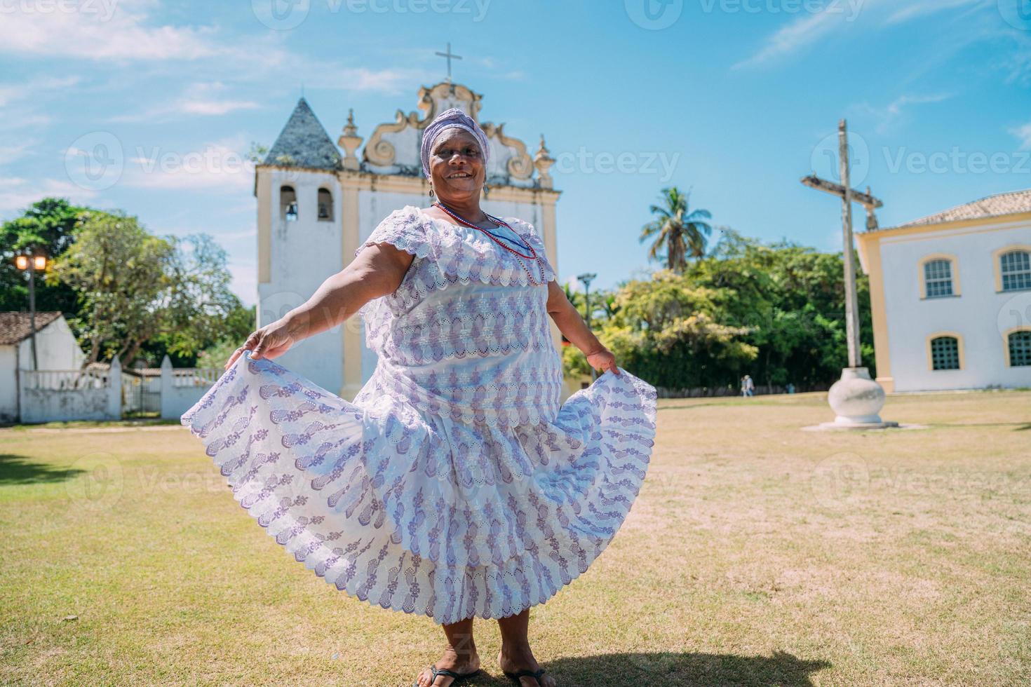 Happy Brazilian woman of African descent dressed in traditional Bahian dress dancing in front of the church photo