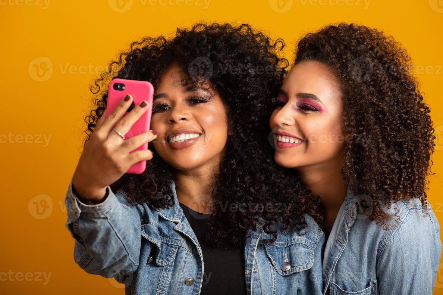 dos chicas afroamericanas tomando fotos selfie con su teléfono celular con fondo amarillo