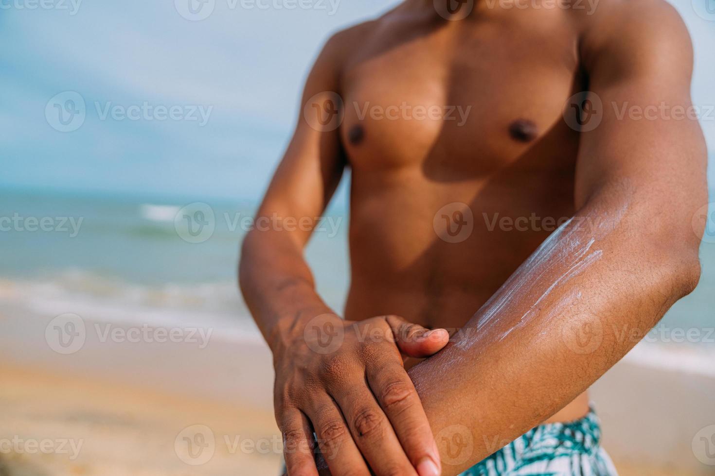 latin american man on the beach. Brazilian model of perfect male abdomen, applying sunscreen. focus on the arm photo