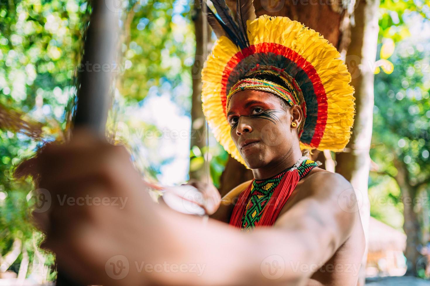 indio de la tribu pataxo usando un arco y una flecha. indio brasileño con tocado de plumas y collar foto