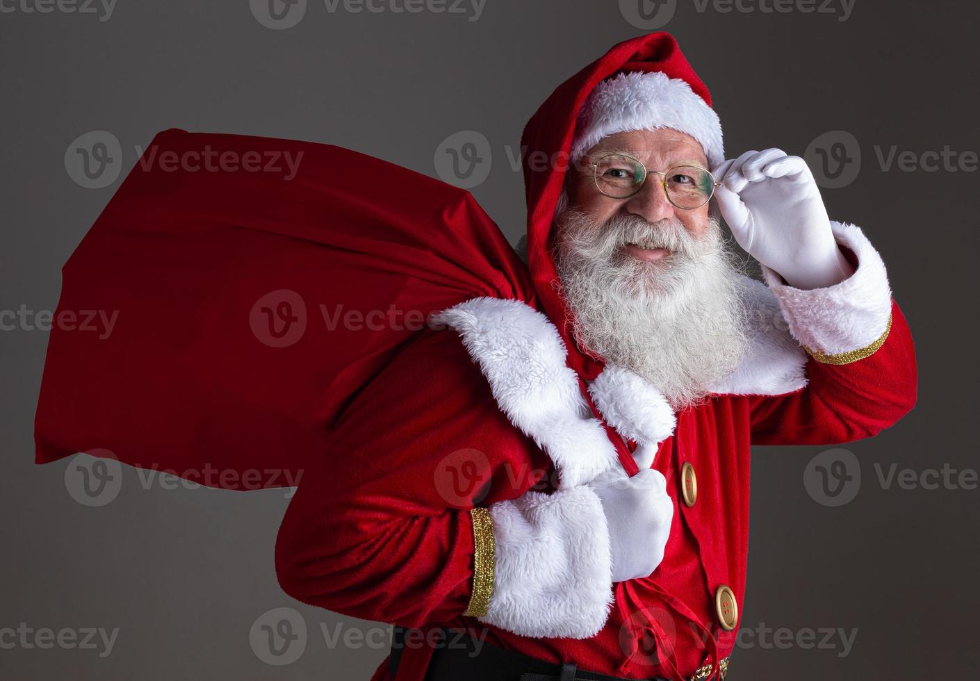 Santa Claus in eyeglasses is looking at camera and smiling, on gray background photo