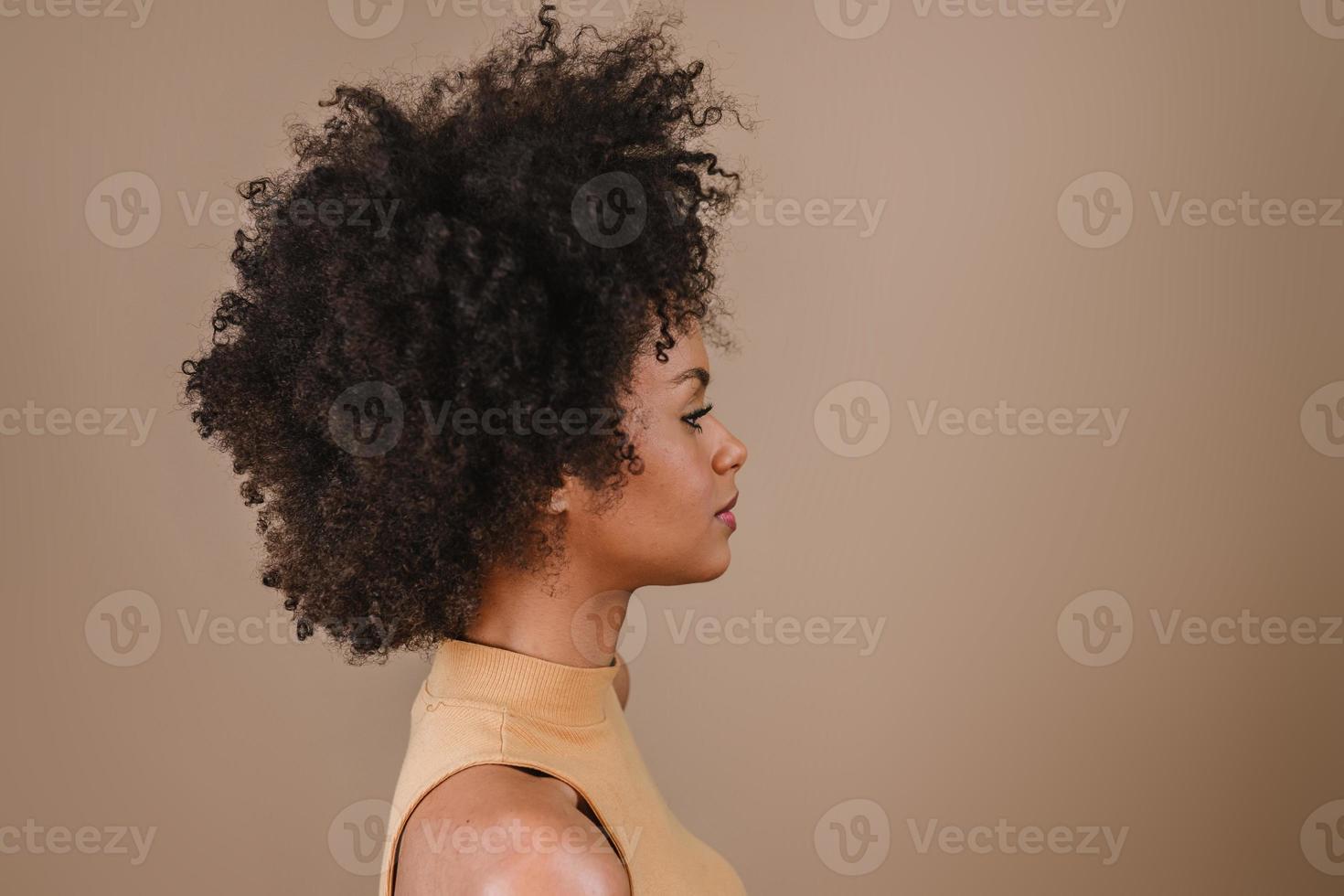 Side a smiling young Latin afro woman. Joy, positive and love. Beautiful african-style hair. Pastel studio background. photo