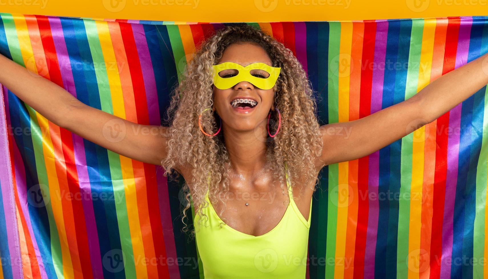 joven mujer de pelo rizado disfrazada disfrutando de la fiesta de carnaval cubierta con la bandera del orgullo lgbt foto