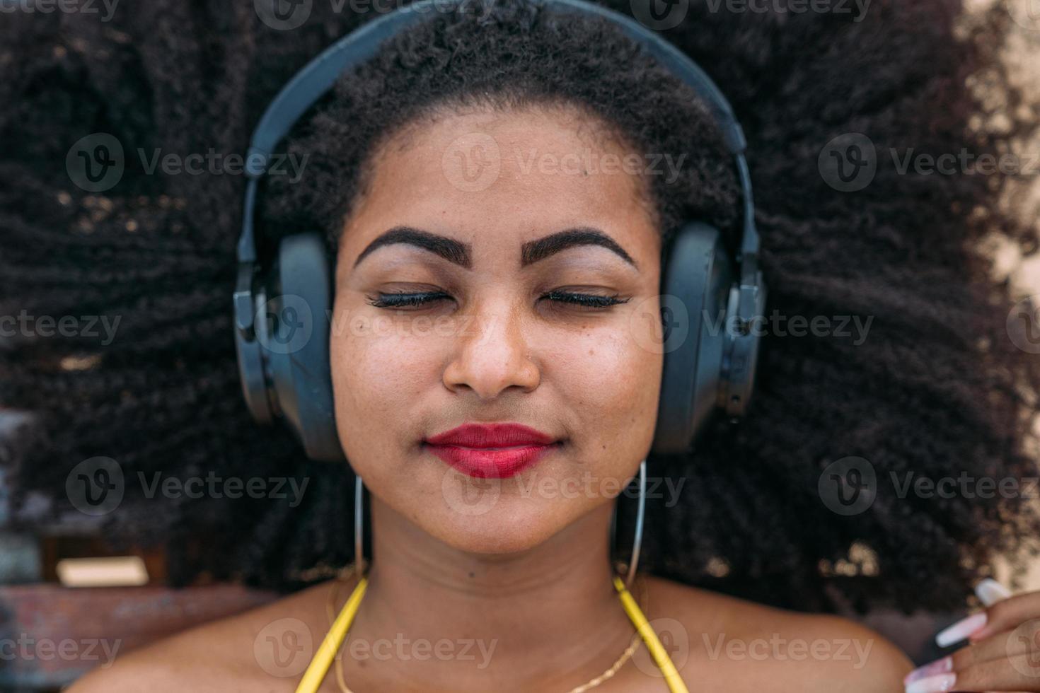 vacaciones de verano, tecnología y concepto de internet. mujer latinoamericana escuchando música con auriculares y tomando el sol en la playa foto