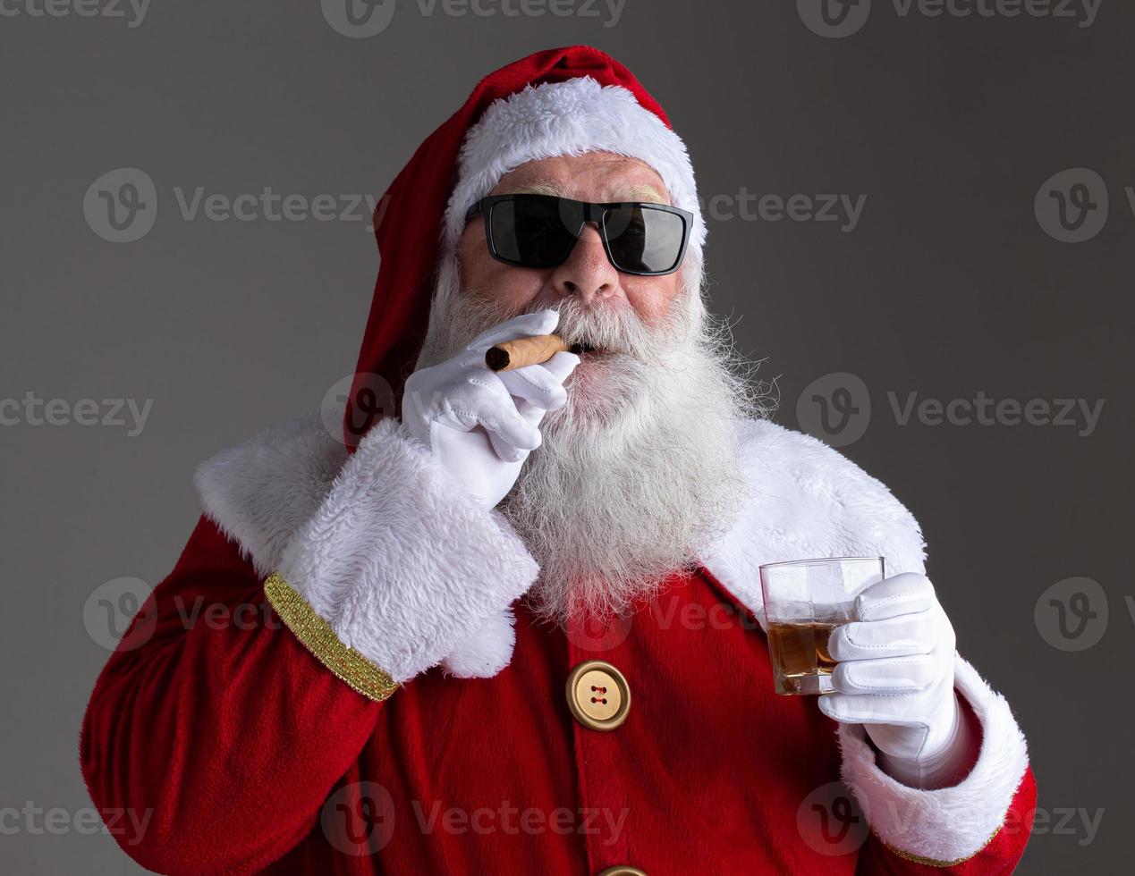 Santa Claus wearing sunglasses smoking a cigar and drinking whisk on dark background photo