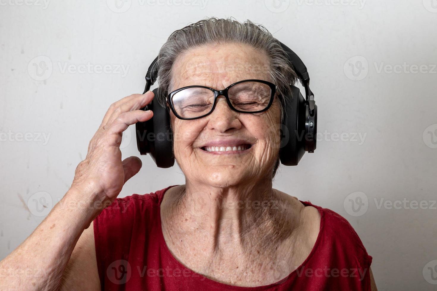 Funny old lady listening music and dancing on white background. Elderly woman wearing glasses dancing to music listening on his headphones. photo