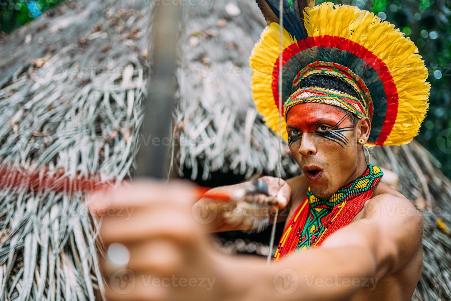 indio de la tribu pataxo usando un arco y una flecha. indio brasileño con tocado de plumas y collar foto