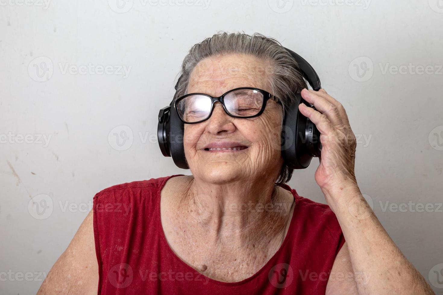 Funny old lady listening music and dancing on white background. Elderly woman wearing glasses dancing to music listening on his headphones. photo