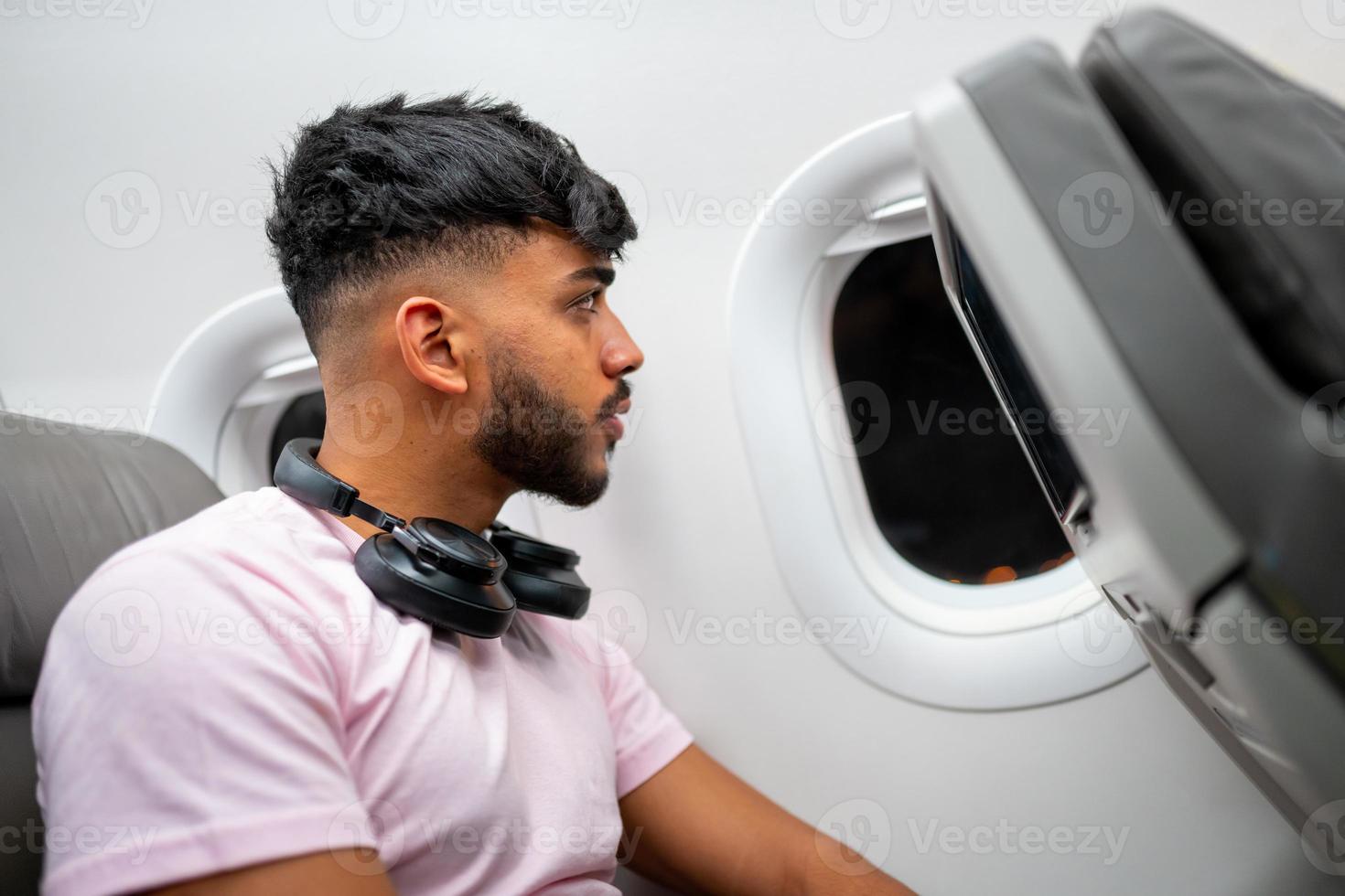 Passenger on the plane, looking at the window. Latin american man in the airplane cabin, with headphones. photo