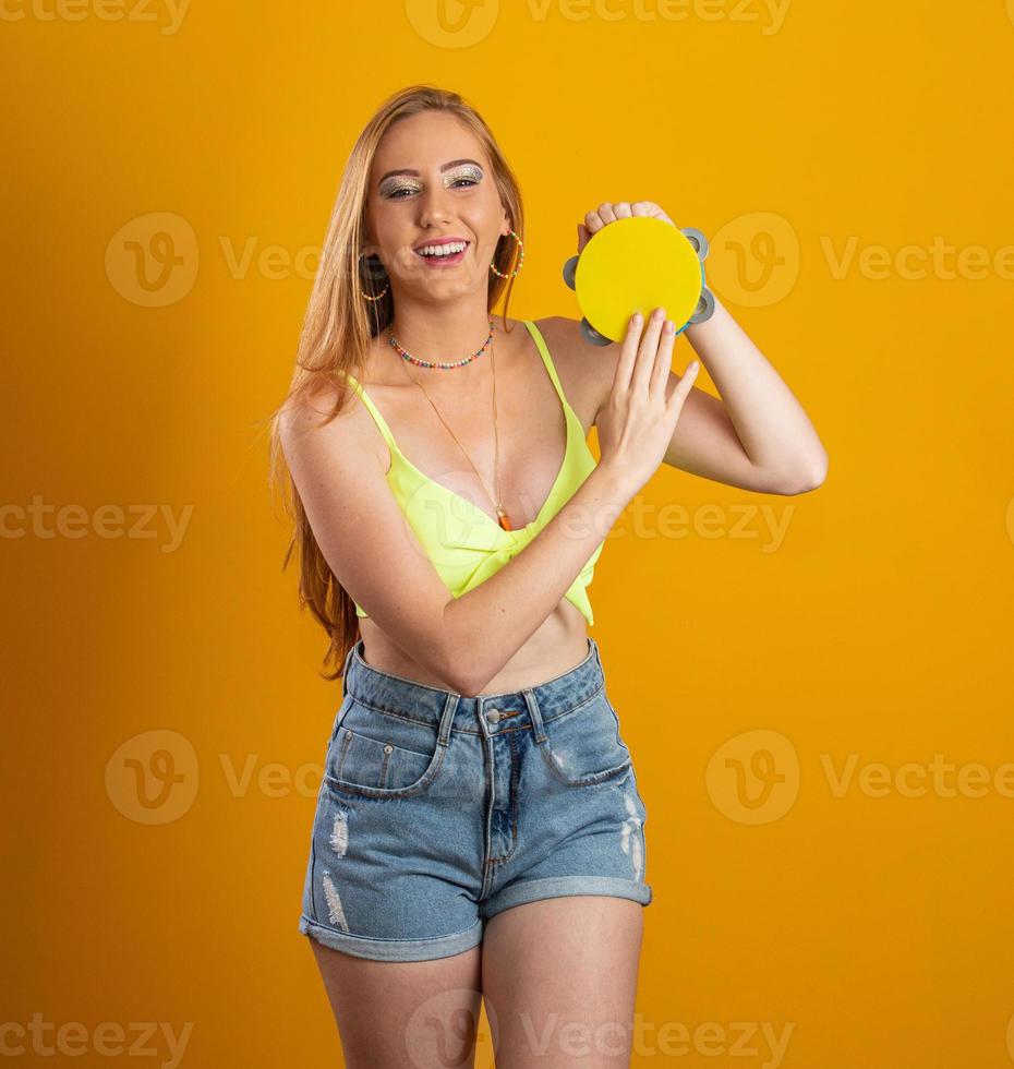 Blond longhaired woman with a toy tambourine in hands. On yellow background. Brazilian girl. Carnival. Rio. photo
