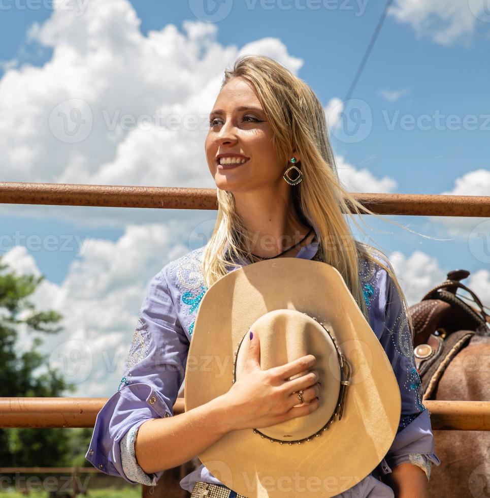 Beautiful blonde cowgirl with hat standing near the horse ranch background photo